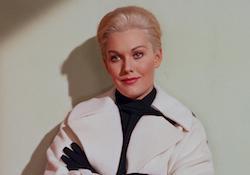 Kim Novak looks on as she leans against white background