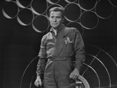 William Shatner standing in a jumpsuit. 