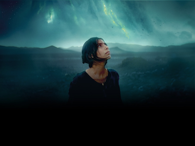 A person looking up at dark, cloud-filled sky. 