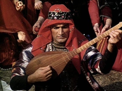 A man playing a stringed instrument and wearing a headdress.