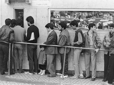 A line of men standing outside a movie theater.