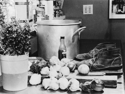A countertop holding onions, garlic, a pair of shoes, and a large pot.