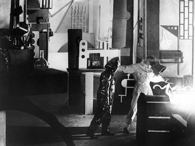 Two people in welding suits in a modernist interior.