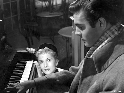 A woman watching a man play a piano.