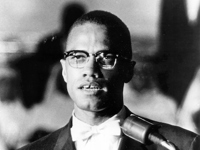 Malcolm X speaking at a microphone.