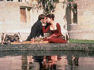 A man and woman sitting and looking at each other romantically by a pond.