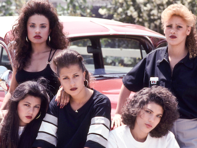 Five women posing in front of a car.