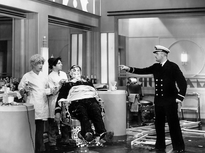 A boat captain pointing at the Marx brothers who are impersonating barbers.