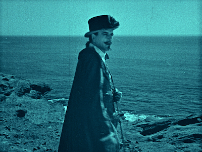 A man in period costume standing by the ocean. 