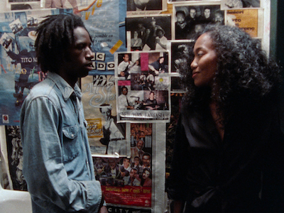 Two people talking in a room plastered with posters.