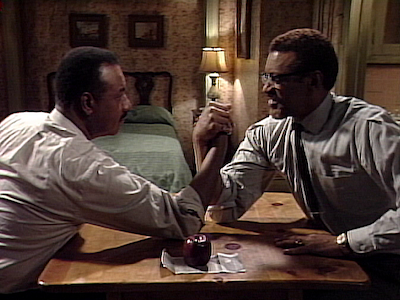 A fictional Martin Luther King Jr. and Malcolm X arm wrestling in a room. 