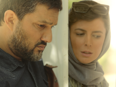 A man and a woman standing on the opposite sides of a door, both looking down.