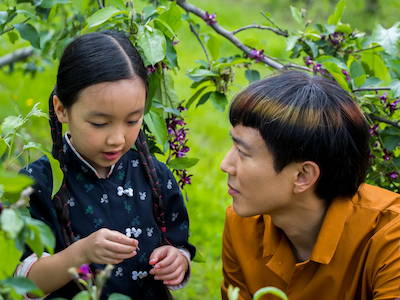 A man kneeling next to a young girl under a tree.