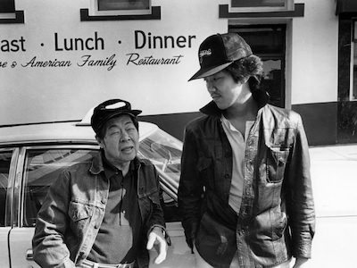 Two men leading against a car outside a Chinese American restaurant.