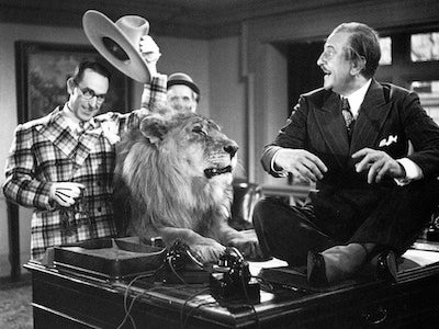 Harold Lloyd tipping a hat with a lion by his side, startling a man.