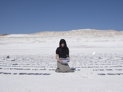 A woman surround by sheets of paper in a desert landscape.