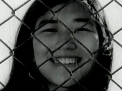 A young woman smiling behind a chainlink fence.