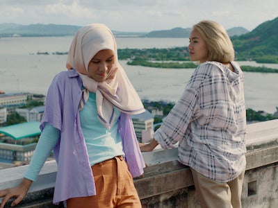 Two women leaning against a wall, with the sea in the background.