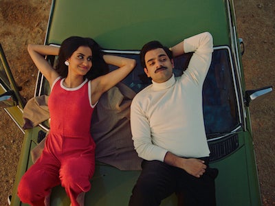 Two people lying on top of a car.