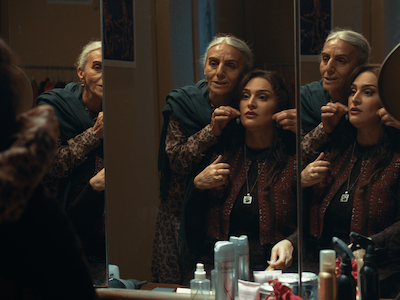 A senior woman holding a necklace around the neck of a younger woman in front of a mirror.