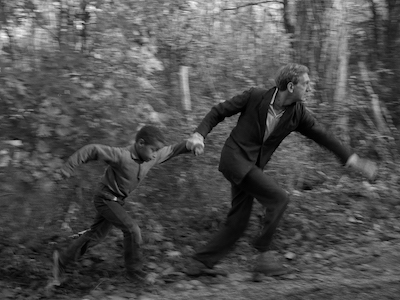 A boy and man holding hands and running among trees.