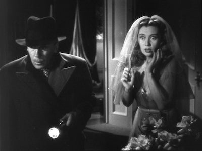 A frightened Joan Blondell wearing a wedding veil next to a man holding a flashlight.