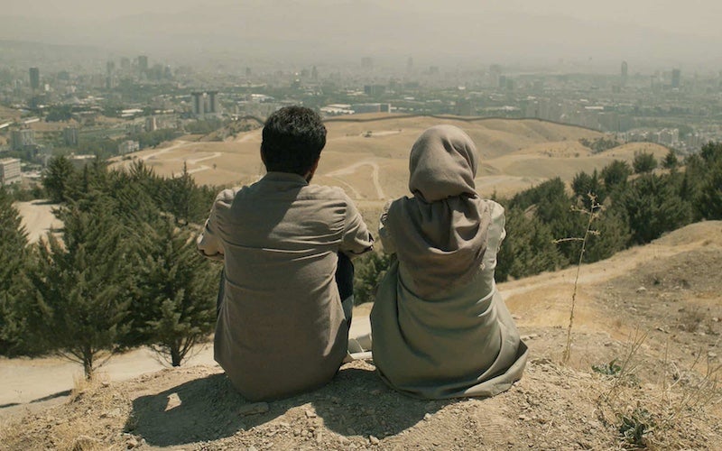Two people sitting on soil and overlooking a landscape and city.