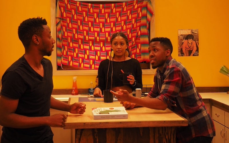 Three young adults talking around a kitchen table.
