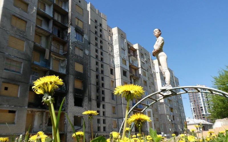 A young adult standing on monkey bars near a bomb-damaged building.