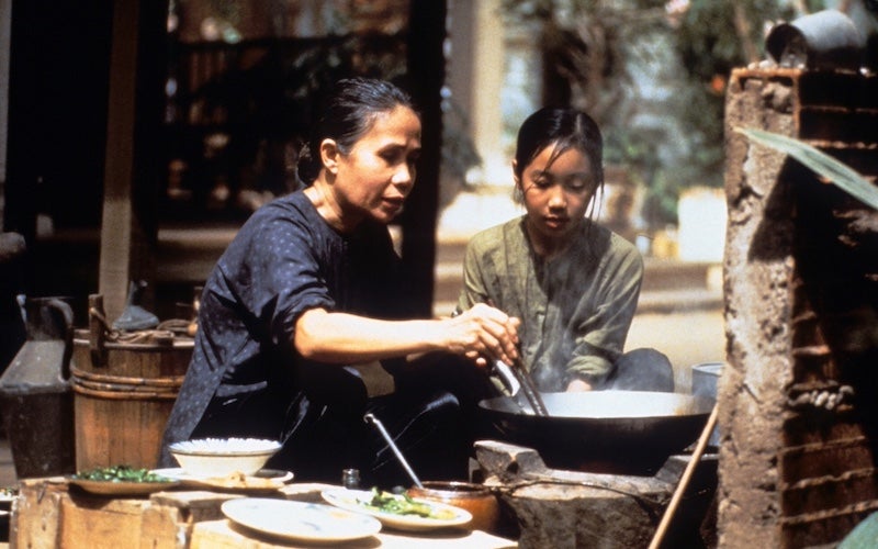 A young girl watching an older woman cook.
