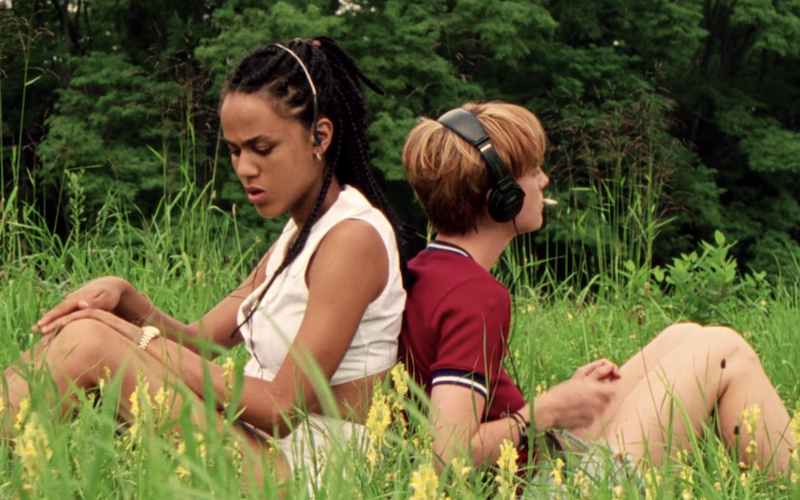 Two young women sitting in a field, sitting back to back.