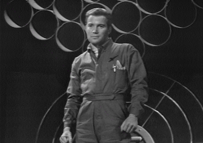 William Shatner standing in a jumpsuit. 