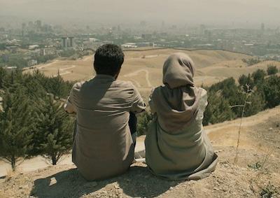 Two people sitting on soil and overlooking a landscape.