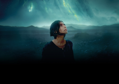 A person looking up at dark, cloud-filled sky. 