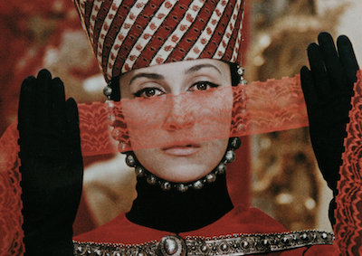 A person in elaborate costume holding a strip of lace in front of their face.