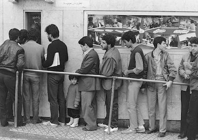 A line of men standing outside a movie theater.