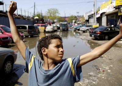 A kid standing with his arms outstretched next to an auto mechanic shop.