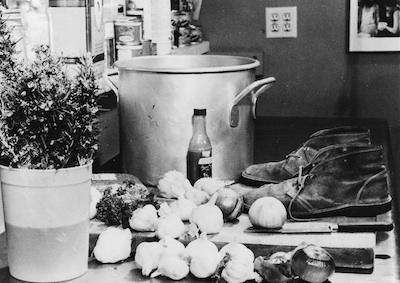 A countertop holding onions, garlic, a pair of shoes, and a large pot.