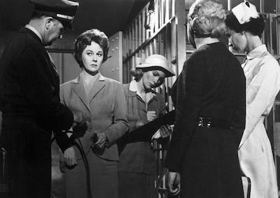 A woman in a jail with a police officer, nurse and other staff.