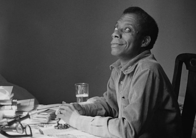 James Baldwin sitting at a table and smiling.