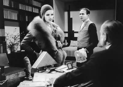 Greta Garbo facing a man seated at a desk in an office.