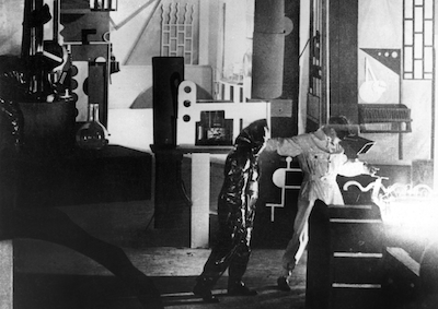 Two people in welding suits in a modernist interior.