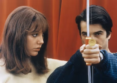 A woman looking at a man holding a bow and arrow.