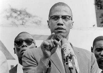 Malcolm X speaking at a podium.