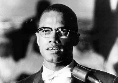 Malcolm X speaking at a microphone.