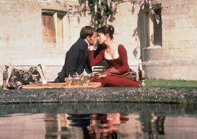 A man and woman sitting and looking at each other romantically by a pond.