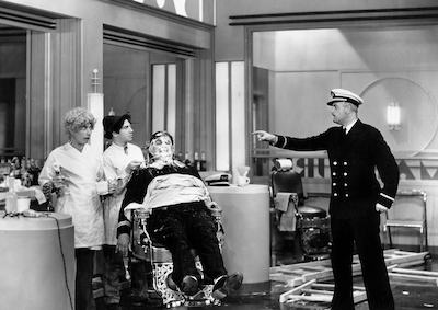A boat captain pointing at the Marx brothers who are impersonating barbers.