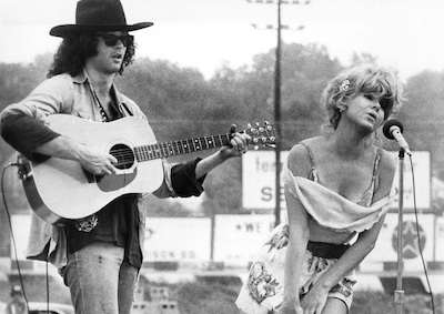 A woman singing into a microphone next to a man playing guitar.