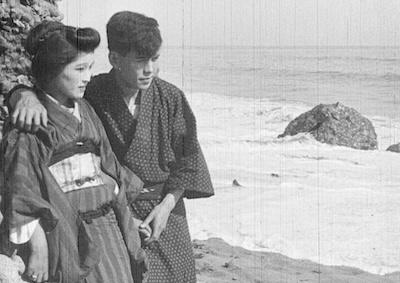 A Japanese woman and man standing by the ocean. 