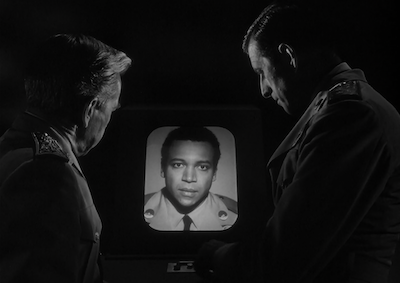 Two men looking at a monitor that shows a man's face.
